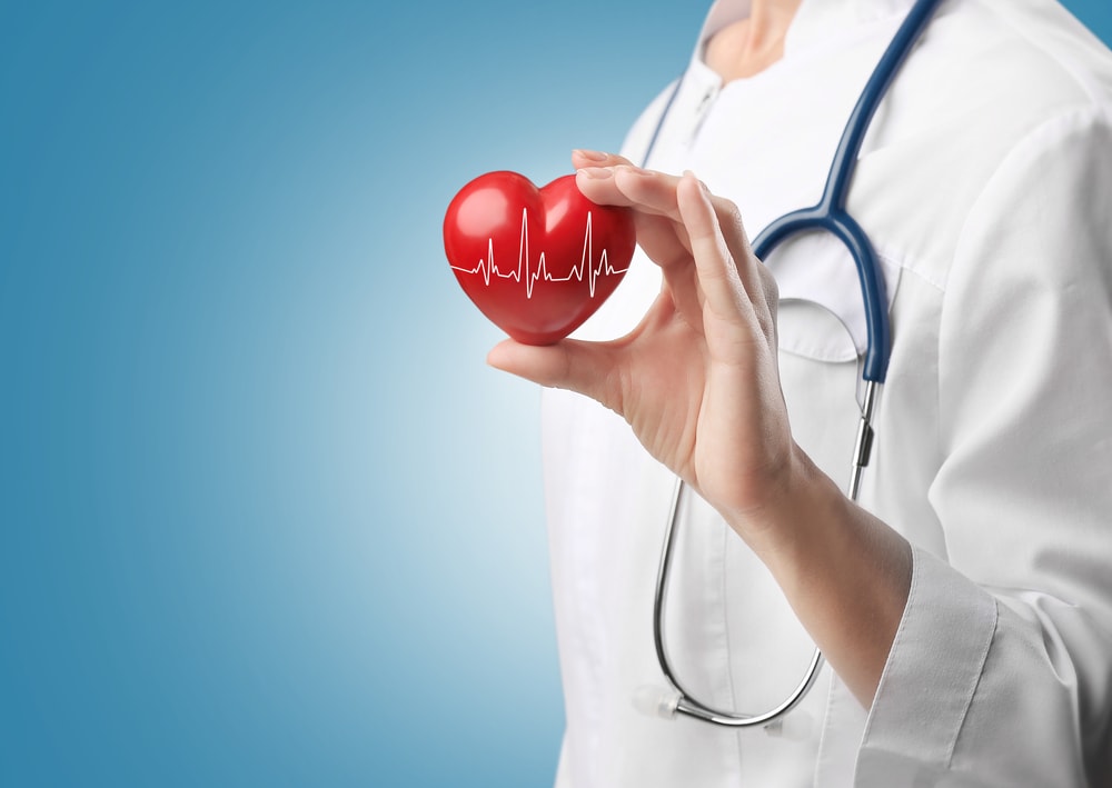 Доктор в бяла роба със стетоскоп на врата, който държи червено пластмасово сърце